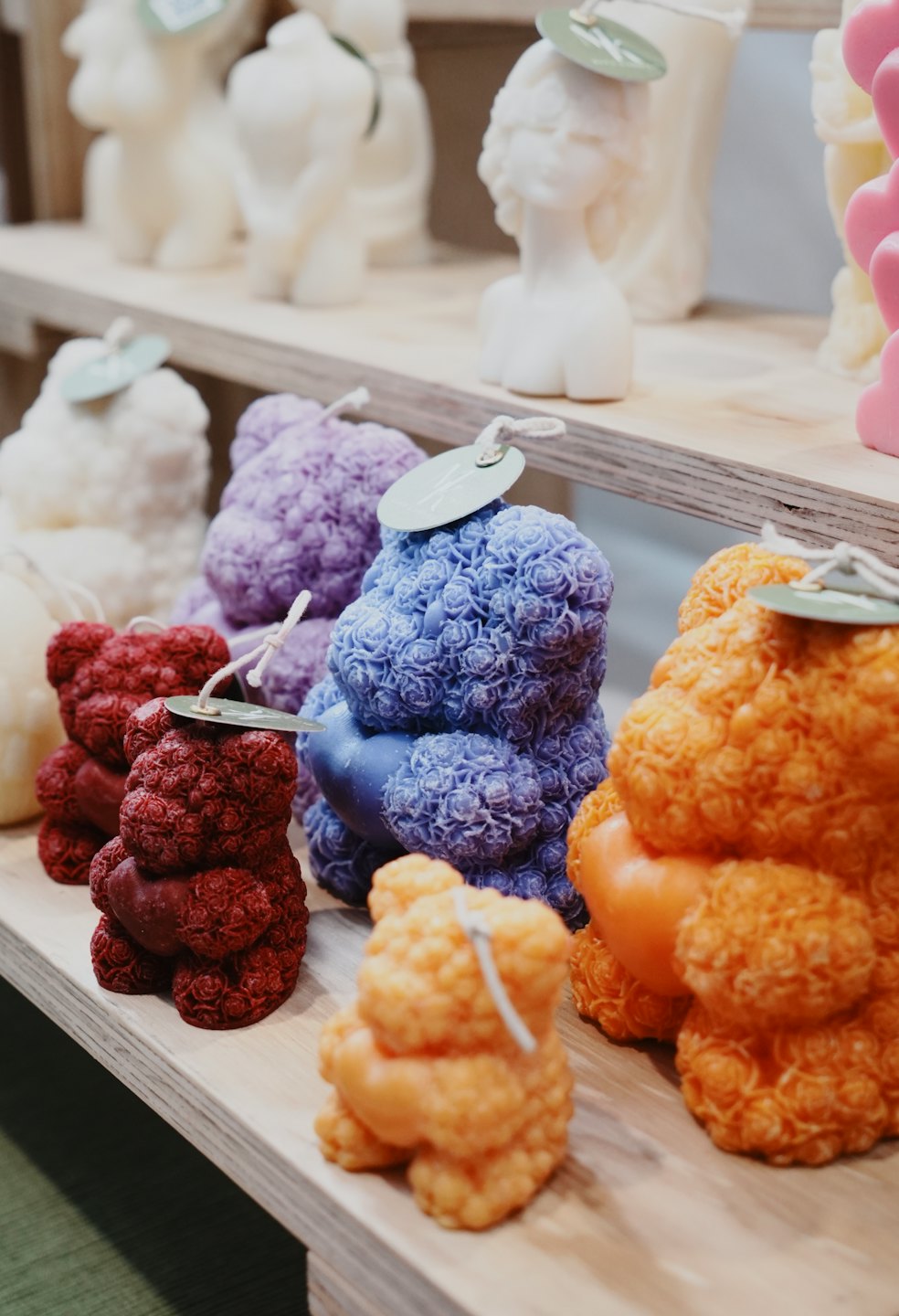 Decorative shaped candles rest on light wooden store shelves.