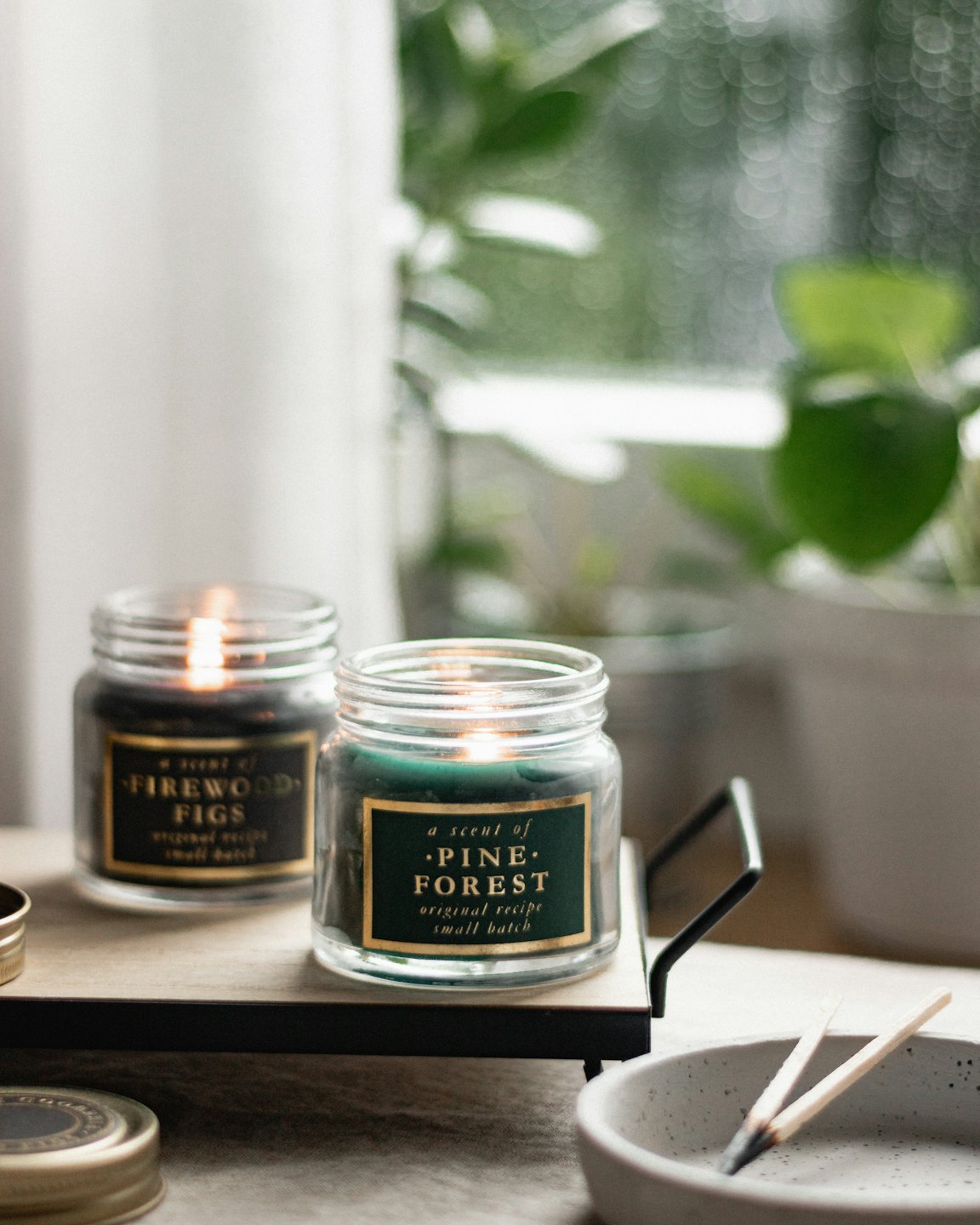 Two scented candles displayed on a wooden tray with matchsticks.