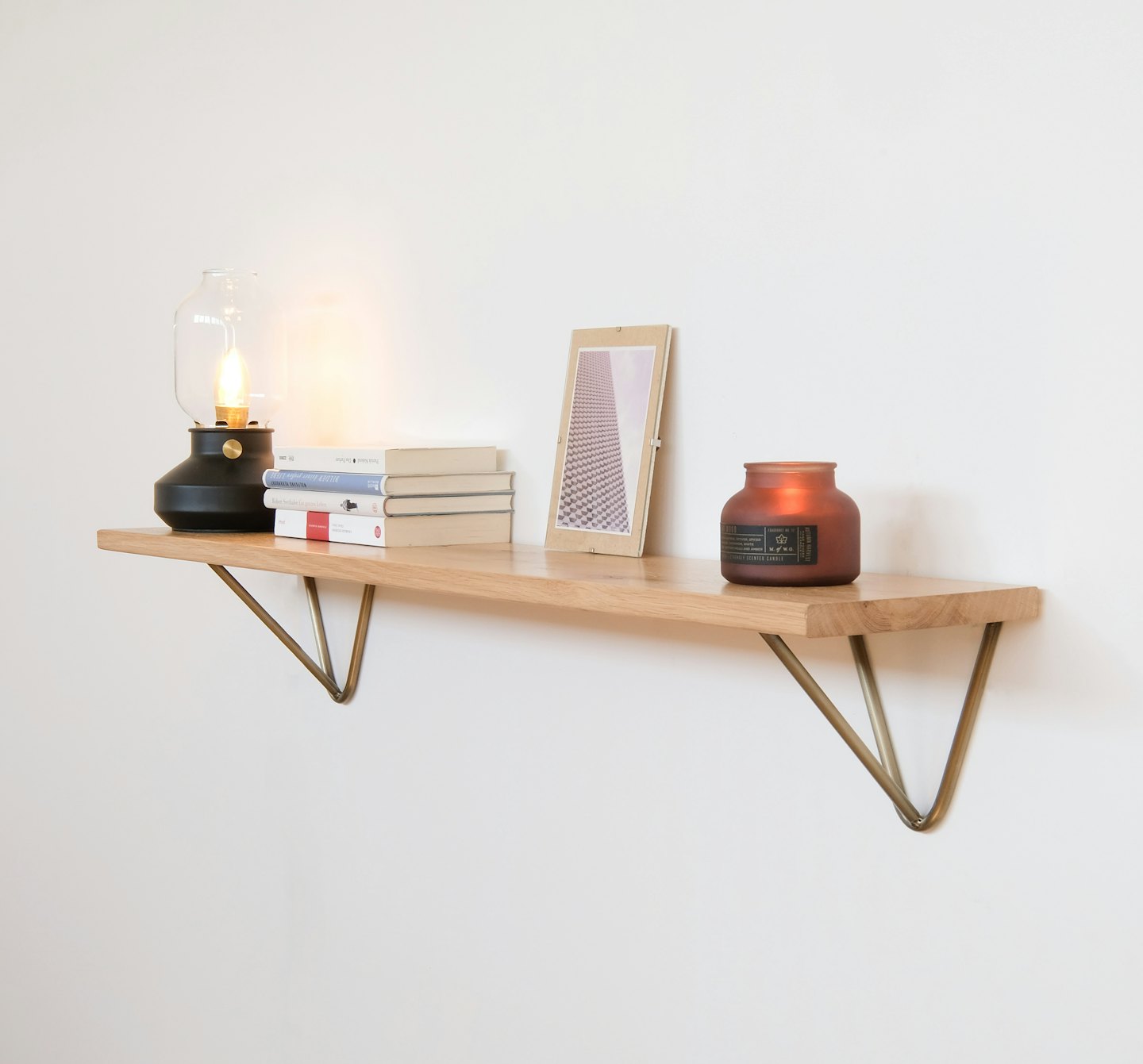 Wooden shelf with lamp, books, and candle on white wall.