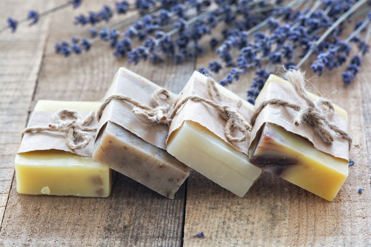Four bars of handmade soap on a wooden surface with lavender.