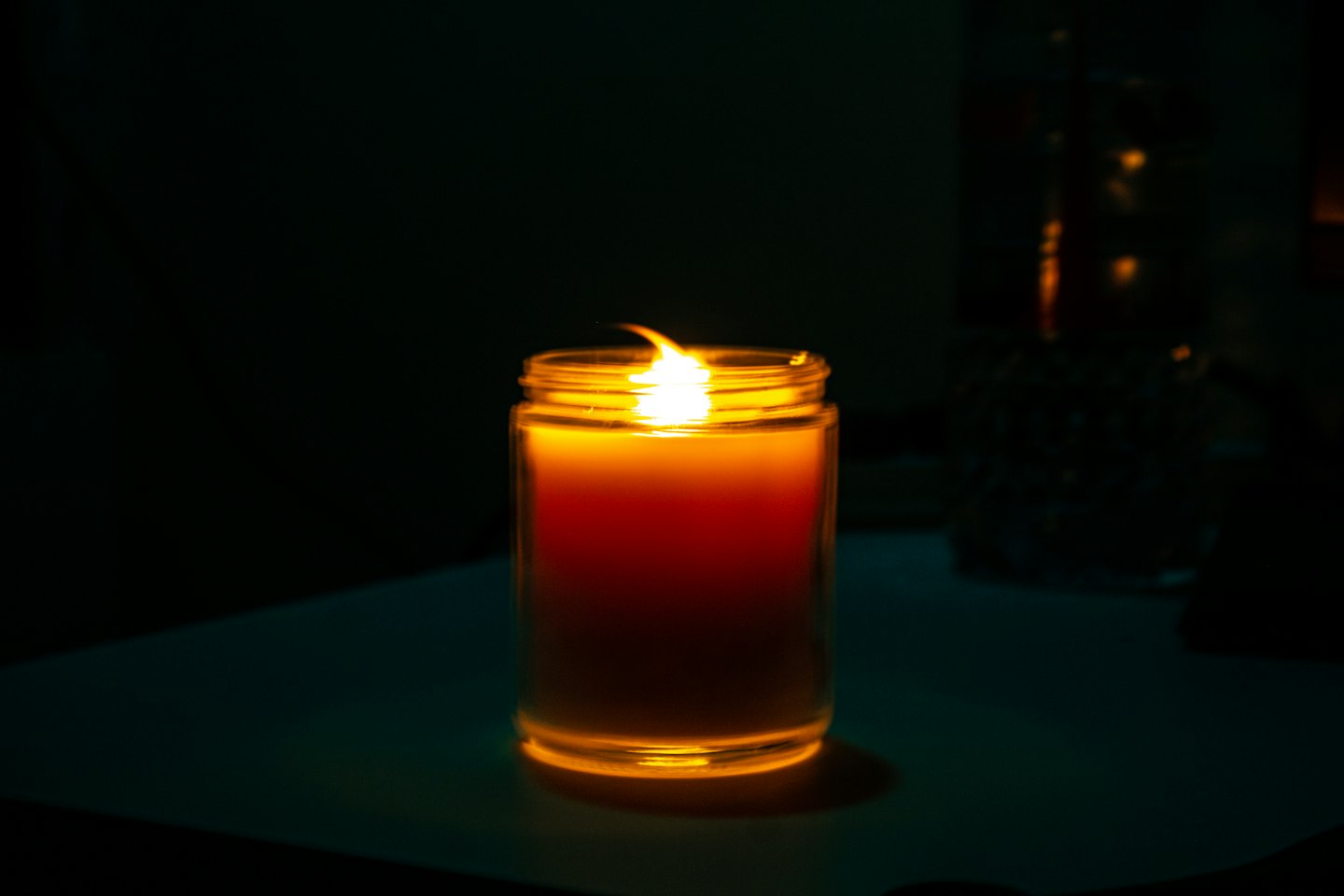 A lit candle in a glass jar glows warmly.